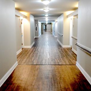 A well-lit corridor featuring wooden flooring and doors along the walls.