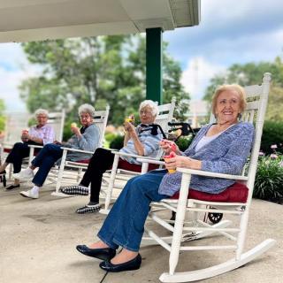 A group of elderly women relaxing on rocking chairs on a porch.