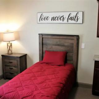 A cozy bedroom with red bedding, wooden furniture, and a decorative sign above the bed.