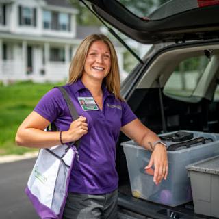 A cheerful individual stands beside their car, ready for the day ahead, with organized bins in the cargo area.