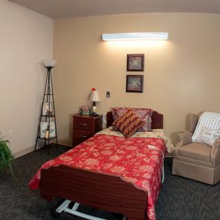 A cozy bedroom with a single bed, lamp, and comfortable chair.