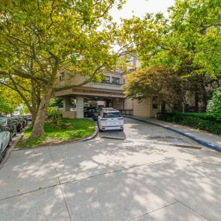A car parked in a driveway surrounded by trees and a residential building.