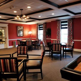 A cozy dining room with multiple tables and chairs, warm lighting, and red walls with large windows.