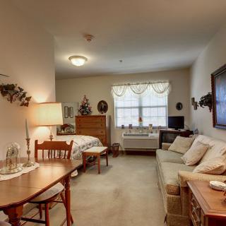 A cozy apartment living space with a bed, sofa, table, and warm lighting.