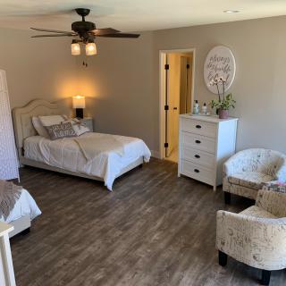 A cozy bedroom with a neatly made bed, dresser, and chairs on wood flooring.