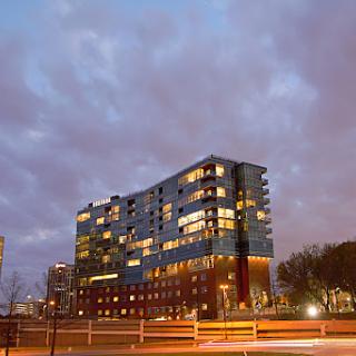 A modern building illuminated at dusk with dramatic clouds in the background.