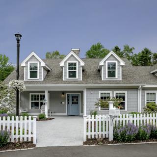 A charming gray house with a white picket fence and landscaped garden.