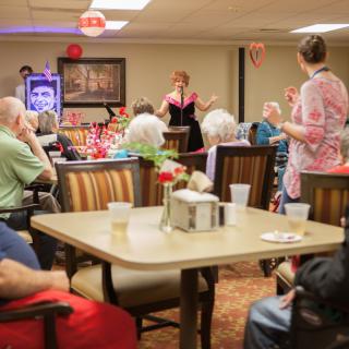 A lively community event at a senior center features a performer entertaining the seated guests.