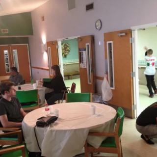 A casual gathering in a community dining area with people seated and standing.