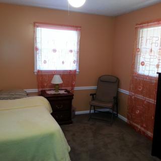 A cozy bedroom featuring a single bed, chair, and wooden furniture with warm-colored walls and curtains.