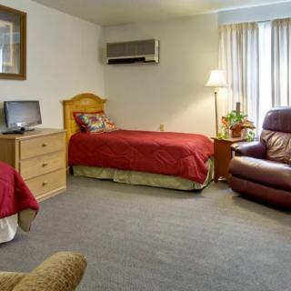 A cozy bedroom with a single bed, television, armchair, and air conditioning unit.
