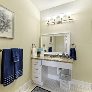 A modern bathroom featuring a white vanity with granite countertop, blue towels, and elegant lighting.