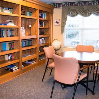 A cozy library corner with bookshelves, a round table surrounded by chairs, and a globe by the window.