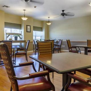 A dining area with several tables and chairs, ceiling fans, and windows providing natural light.