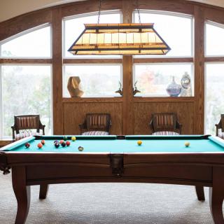 A cozy game room featuring a billiard table with stylish lighting and comfortable seating by large windows.