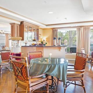 A cozy dining area with a glass table and wooden chairs, adjacent to a kitchen with ample natural light.