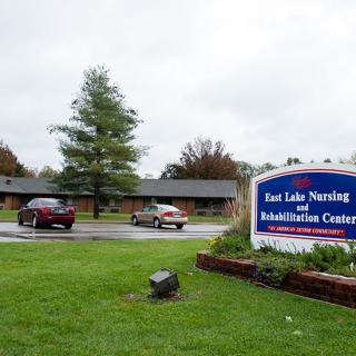 Exterior view of East Lake Nursing and Rehabilitation Center with a parking area and garden.