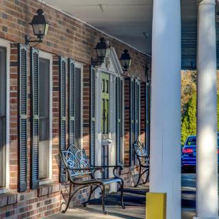 A charming brick building with a covered porch, featuring benches, columns, and decorative shutters.