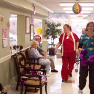 Healthcare workers and residents in a nursing home hallway.
