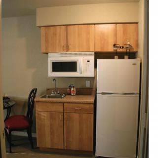 A compact apartment kitchen with a microwave, refrigerator, sink, and wooden cabinets.