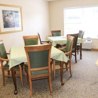 A well-lit dining area with tables and chairs, adorned with green tablecloths, and a painting on the wall.