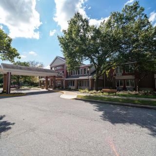 A building with a covered entrance and a driveway surrounded by trees under a partly cloudy sky.