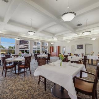 A spacious dining room with elegantly set tables, white tablecloths, and large windows allowing natural light.
