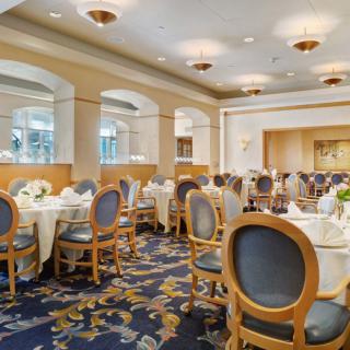 An elegant banquet hall set up for a formal event, featuring round tables with white tablecloths and classical chairs.