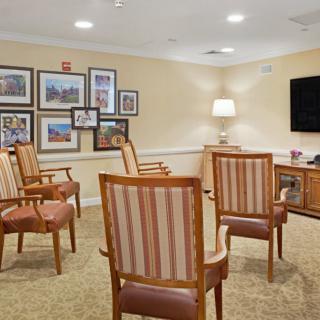 A cozy living room setup with chairs arranged around a television, surrounded by framed photos on the wall.