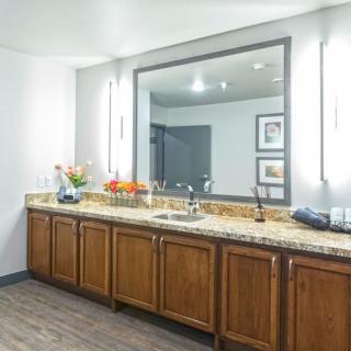 A spacious bathroom featuring a large mirror, granite countertop, and wooden cabinets with modern lighting.