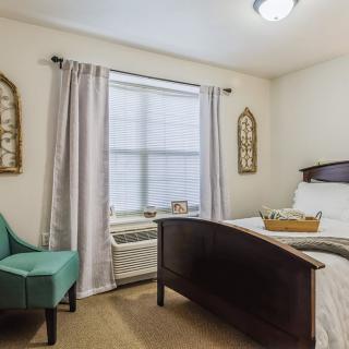 A cozy bedroom with a neatly made bed, teal armchair, and decorative wall art.