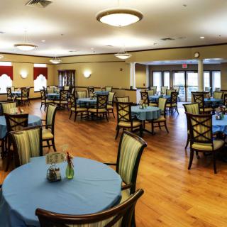 A spacious dining room with neatly arranged tables and chairs, featuring a warm wooden floor and elegant lighting.