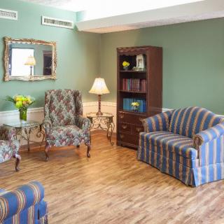 A cozy living room with a striped sofa, patterned chairs, a wooden bookshelf, and a decorative mirror.