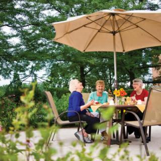 A group of friends enjoying a conversation at a patio table under a large umbrella.