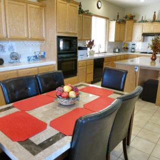 A spacious kitchen and dining area featuring wooden cabinets, a central dining table with red placemats, and modern appliances.
