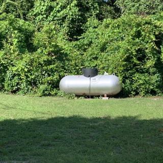 A propane tank placed in a grassy area surrounded by trees and greenery.