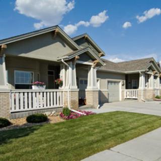 A suburban single-story house with a well-maintained lawn and porch under a blue sky.