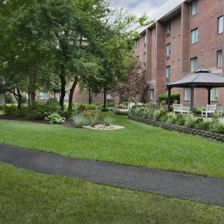 A serene garden with a pathway, surrounded by an apartment building and lush greenery.