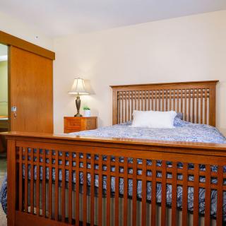 A cozy bedroom with a wooden bed frame and a patterned bedspread, accompanied by a lamp on a bedside table.
