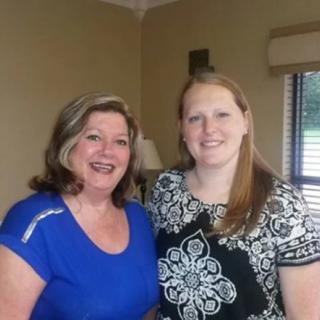 Two women standing together and smiling indoors.