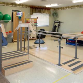 A physical therapy room equipped with parallel bars and various exercise equipment.
