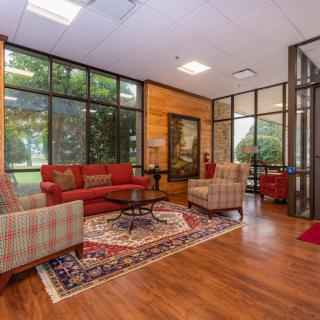 A cozy lobby with red sofas, armchairs, and large glass windows.