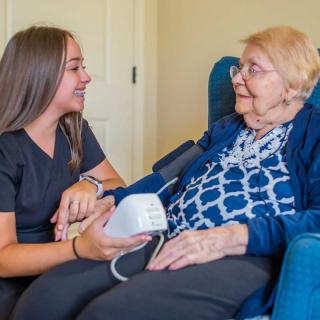 A nurse assists an elderly woman with a blood pressure check, sharing a warm interaction.