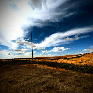 A serene rural landscape featuring a vast field under a dramatic sky with dynamic cloud formations.