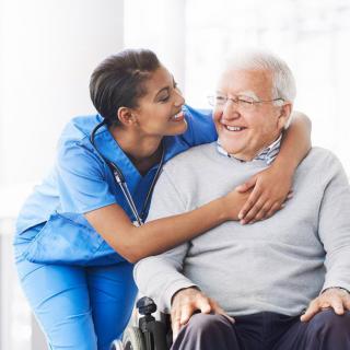 A nurse showing affection and support to an elderly man in a wheelchair.
