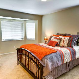 A cozy bedroom with a neatly made bed, featuring colorful pillows and a warm blanket next to a window.