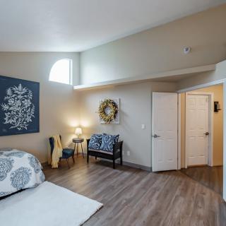 A modern bedroom featuring wood flooring, stylish furniture, and natural lighting with decorative artwork on the walls.