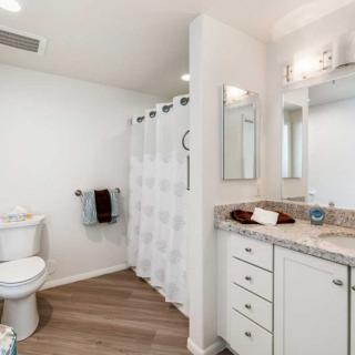 A modern bathroom with white decor and wood flooring, featuring a shower, toilet, sink, and storage cabinets.