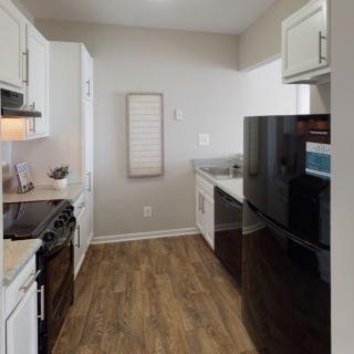 A modern kitchen with white cabinets, hardwood floors, and sleek appliances.