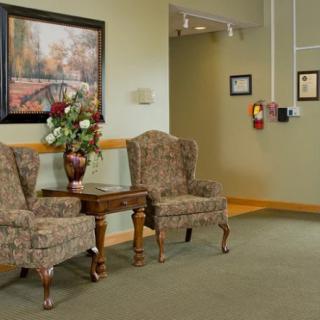 A cozy lounge area with patterned chairs and a small table topped with a vase of flowers, set against a background of soft-colored walls adorned with artwork and certificates.